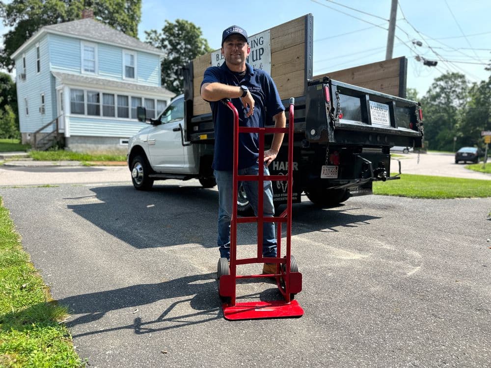 Man with a red hand truck beside a pickup truck outside a house, ready for moving tasks.