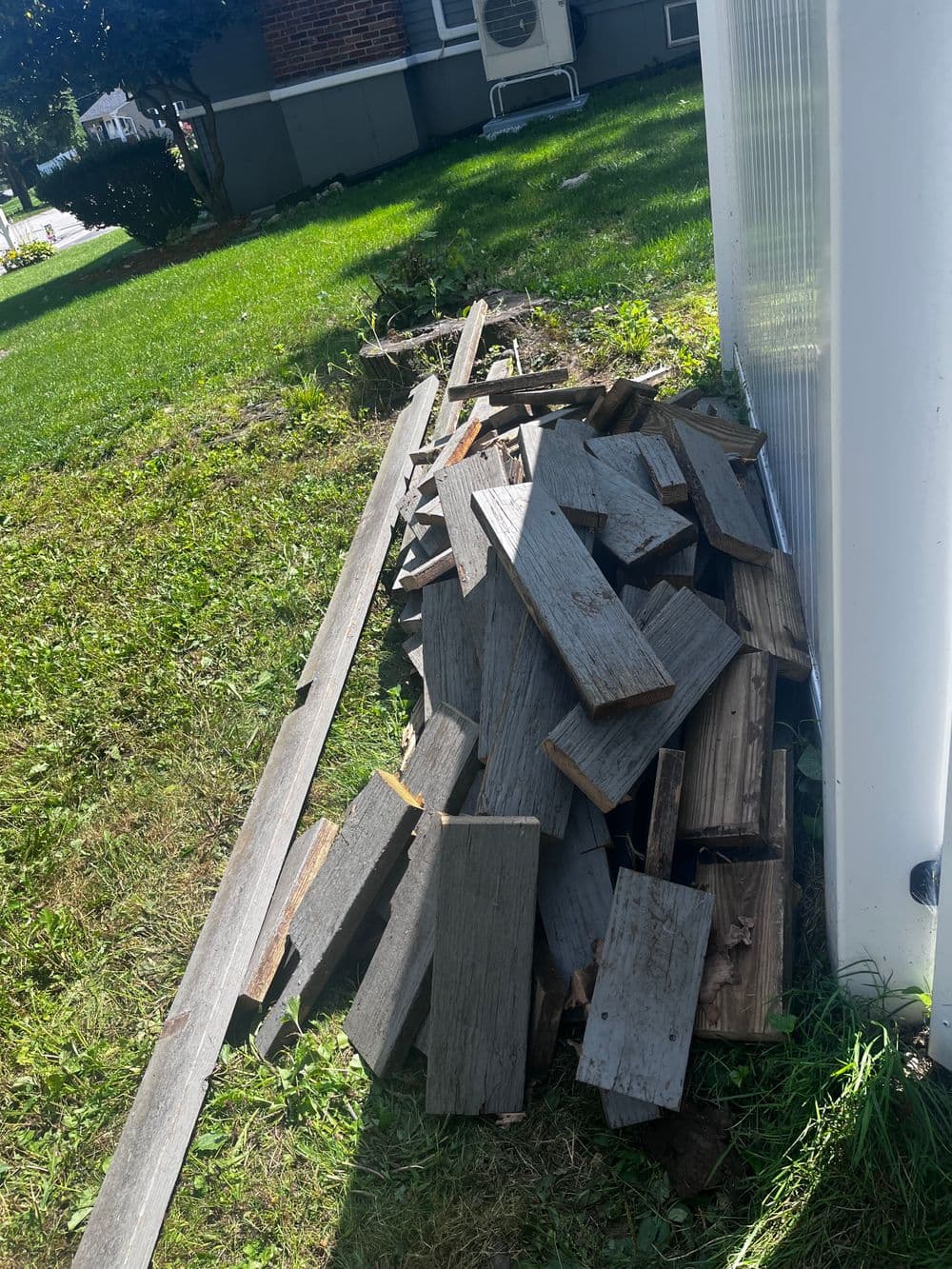 Pile of wooden planks and debris on grassy yard near a building's side.