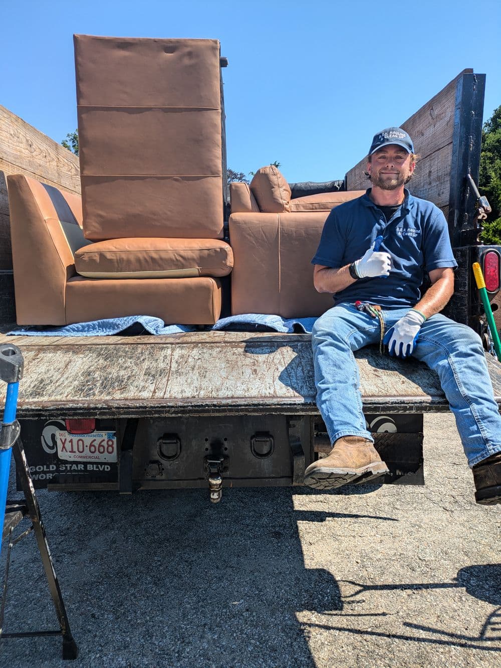 Man giving a thumbs up while sitting on a truck with furniture in the background.