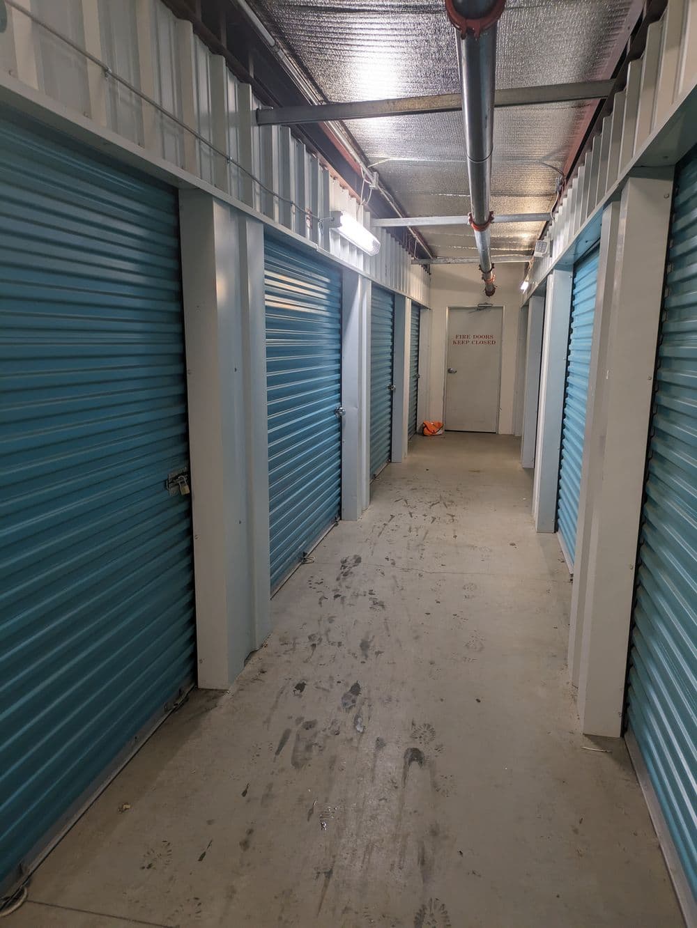 Interior of a storage facility hallway with blue roll-up doors and concrete flooring.